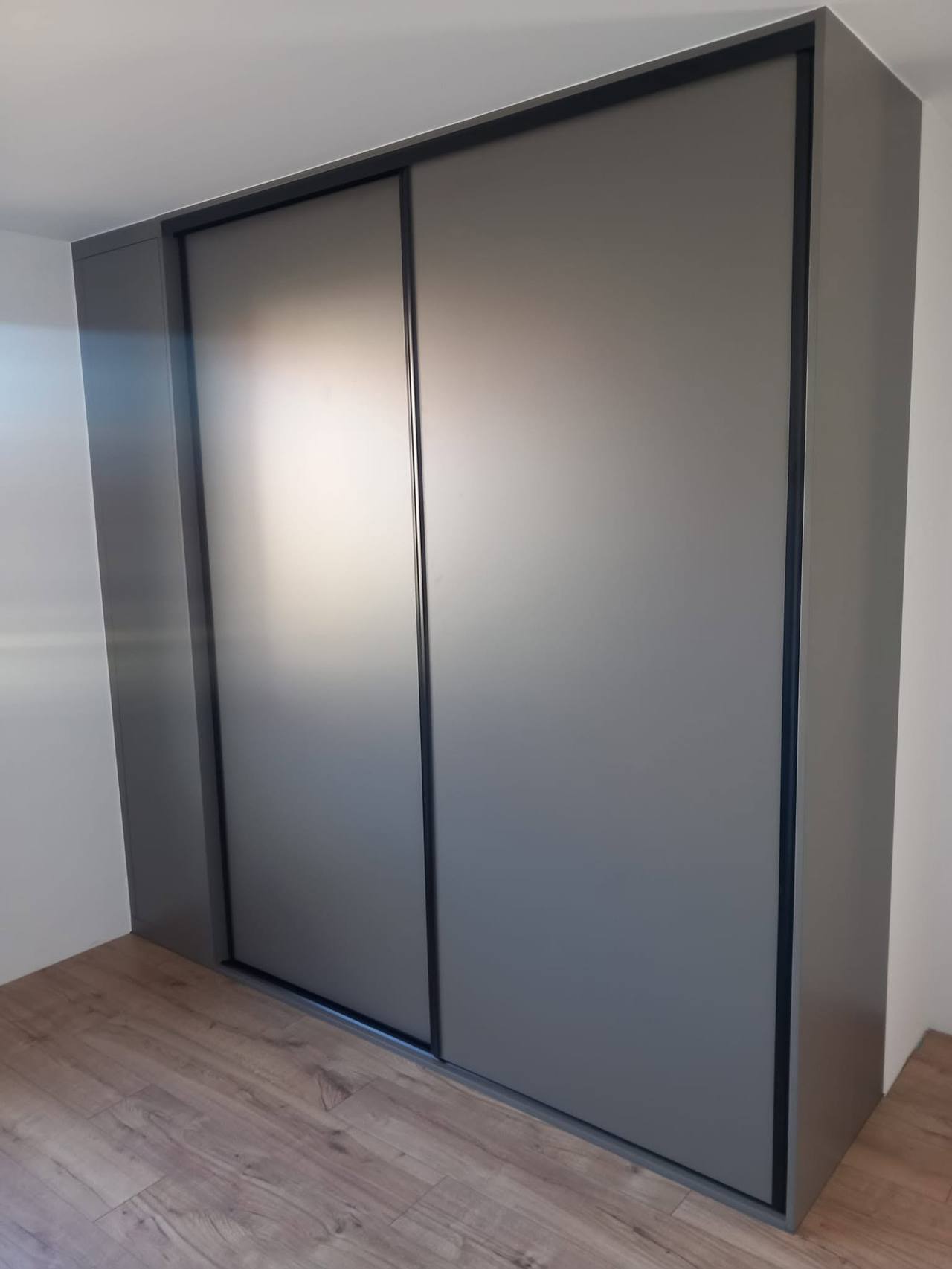 Anthrazitfarbener Schiebetürenkasten mit schwarzen Profilen im Zimmer