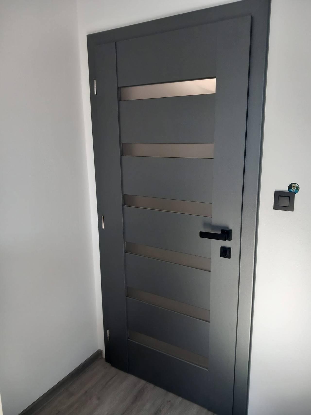 Anthrazitfarbene Tür mit fünf bronzefarbenen Glasbändern über dem Holzboden