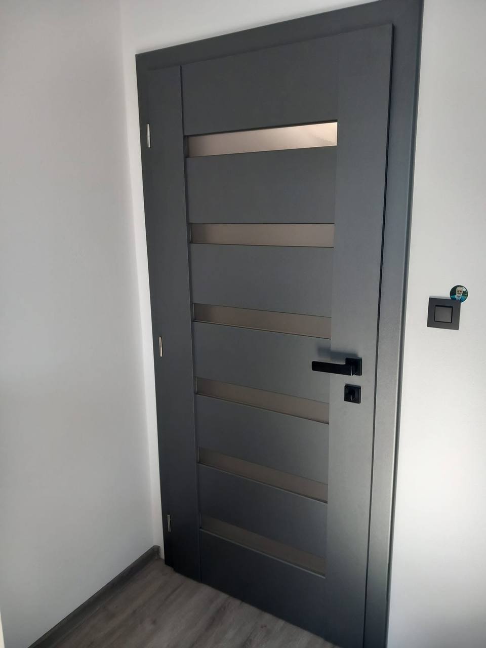 Anthrazitfarbene Tür mit fünf bronzefarbenen Glasbändern über dem Holzboden