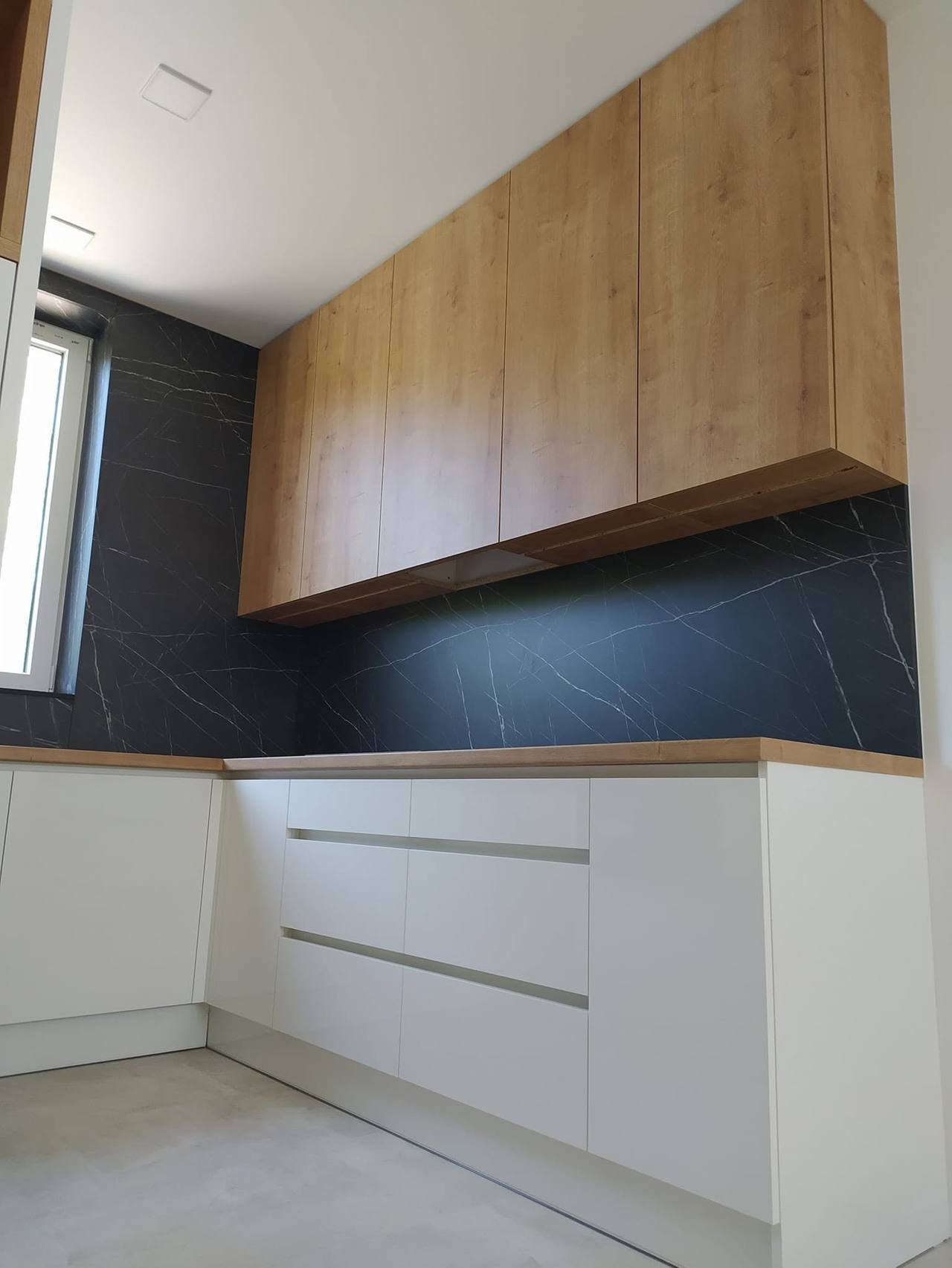 Weiße grifflose Küche mit Eichenboard und schwarzem Marmorspiegel.