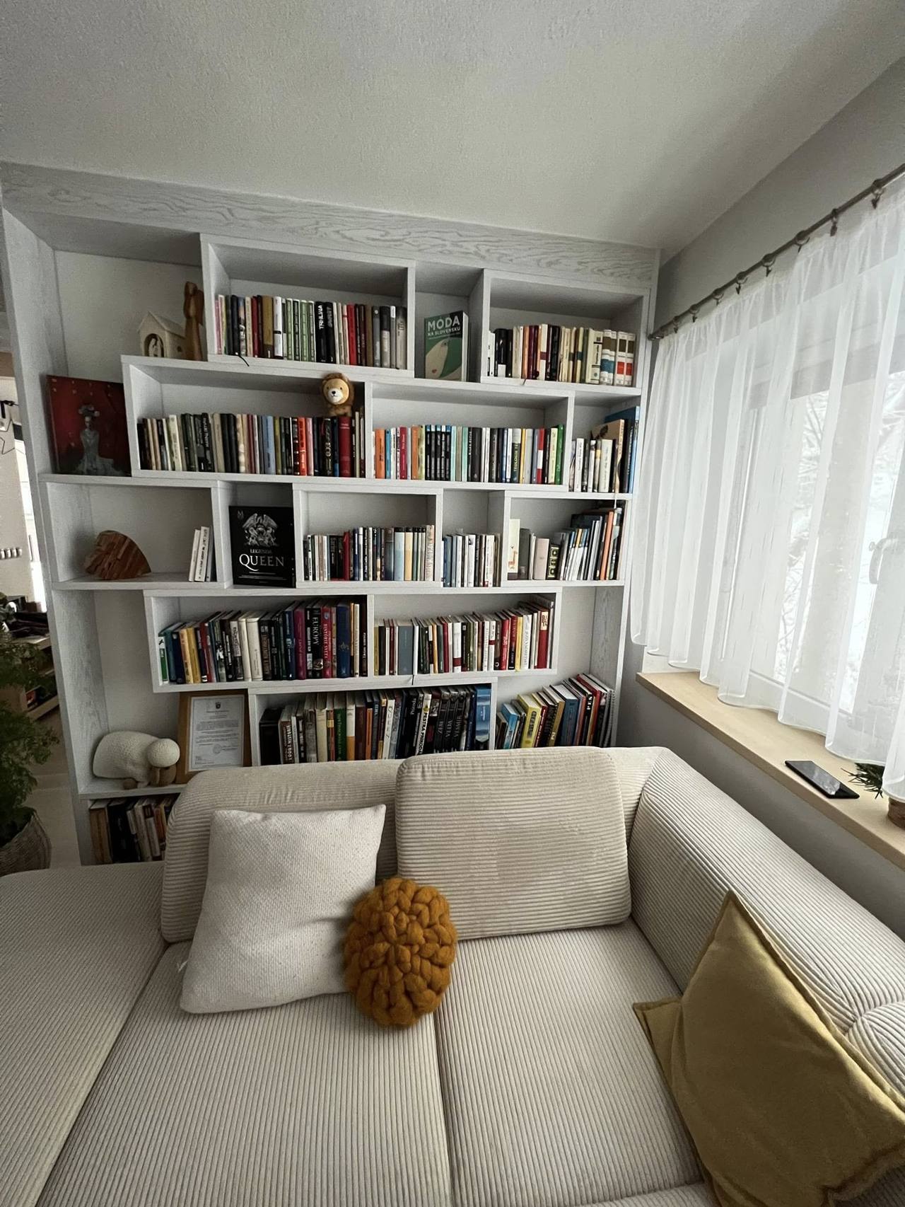 Weißes Bücherregal rund ums Fenster über dem hellen Sofa