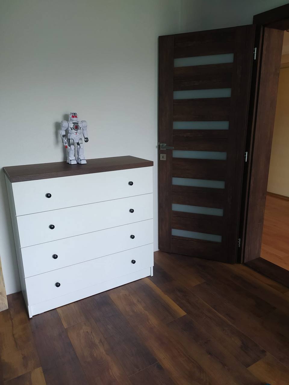 Weiße Kommode mit vier Laden neben dunkler Tür im Zimmer