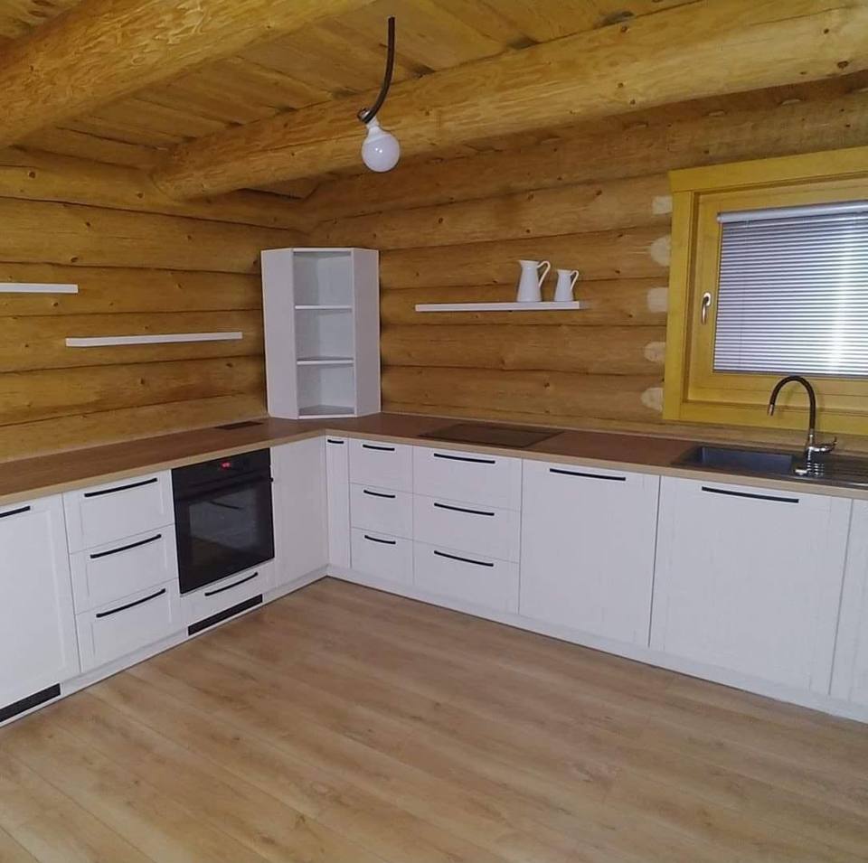 Weiße Eckküche im Blockhaus mit schwarzen Griffen und einem Fenster.