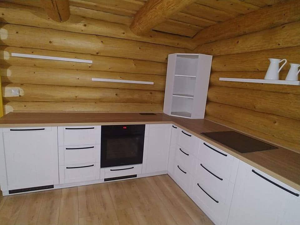 Weiße Küchenzeile an der Holzwand mit offenem Eckregal.