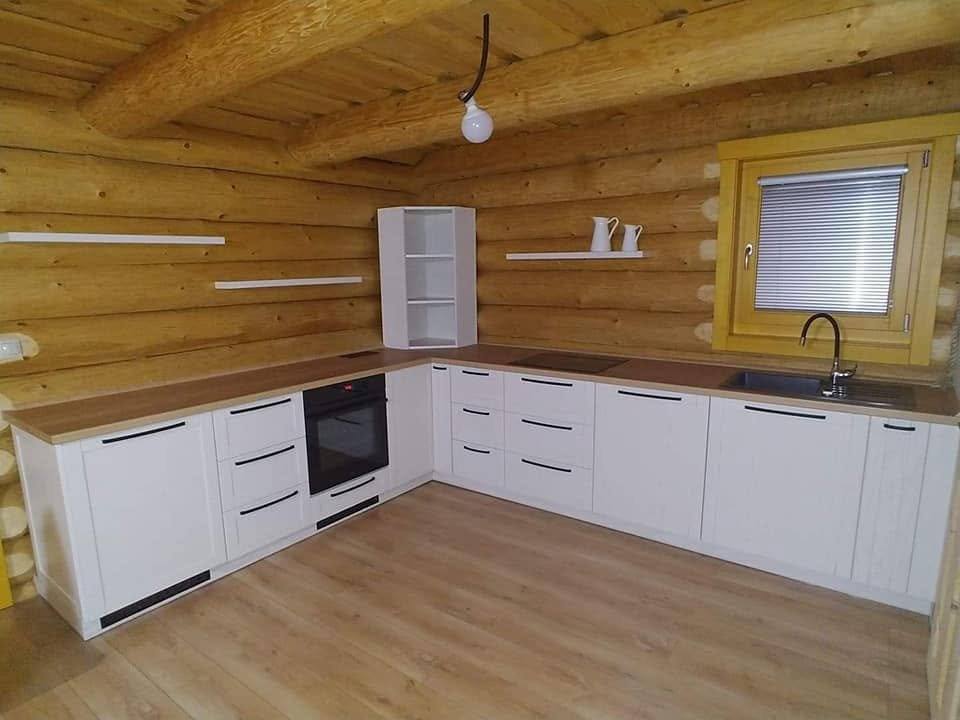 Blick auf die weiße Küche im Blockhaus mit kleinem Holzfenster.