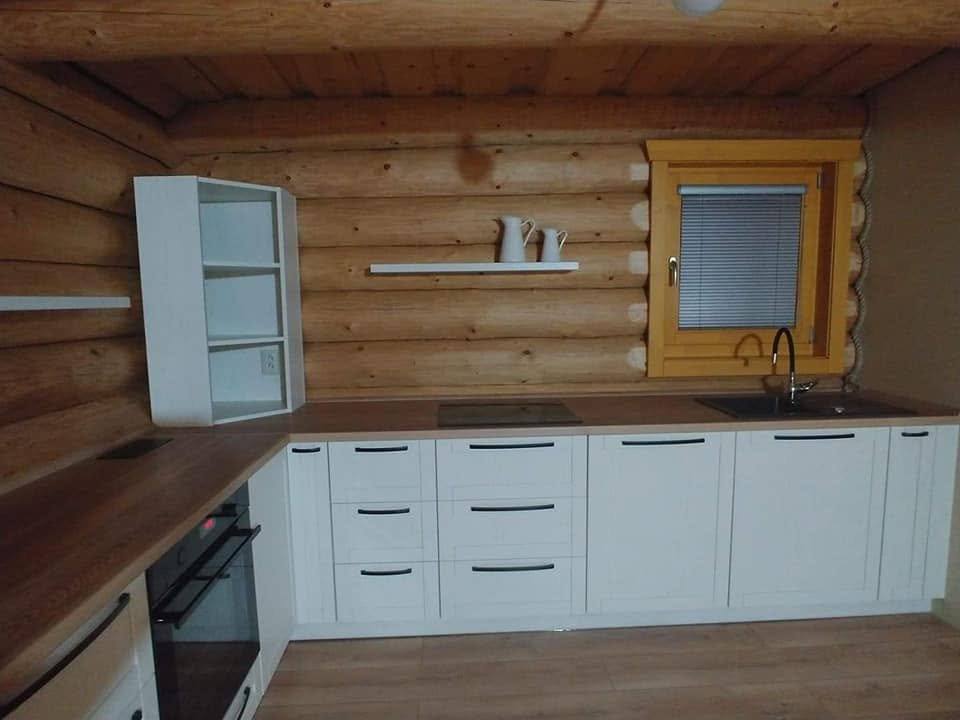 Weiße Küchenzeile an der Blockhauswand mit dunklerer Arbeitsplatte.
