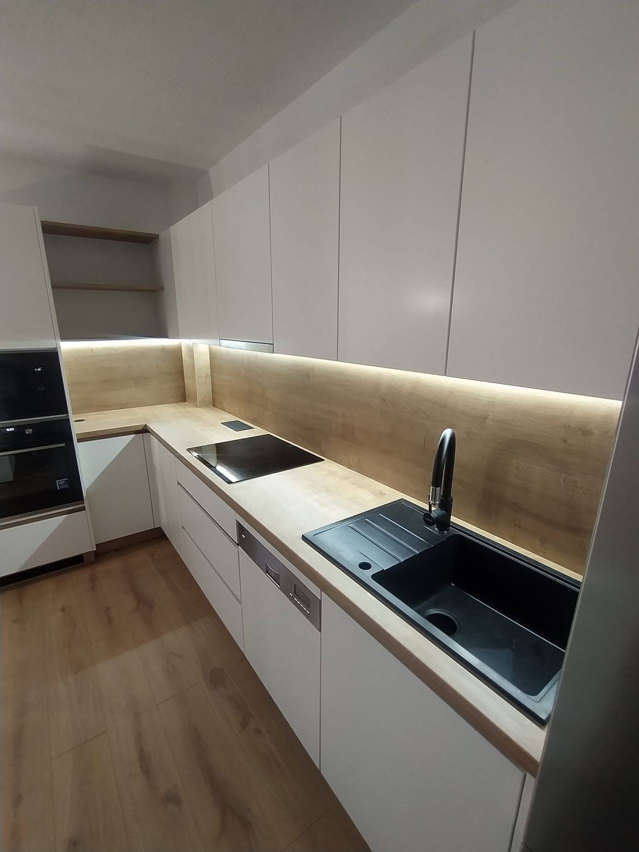 Weiße Küche mit Eichenspiegel, LED-Beleuchtung und schwarzer Spüle.