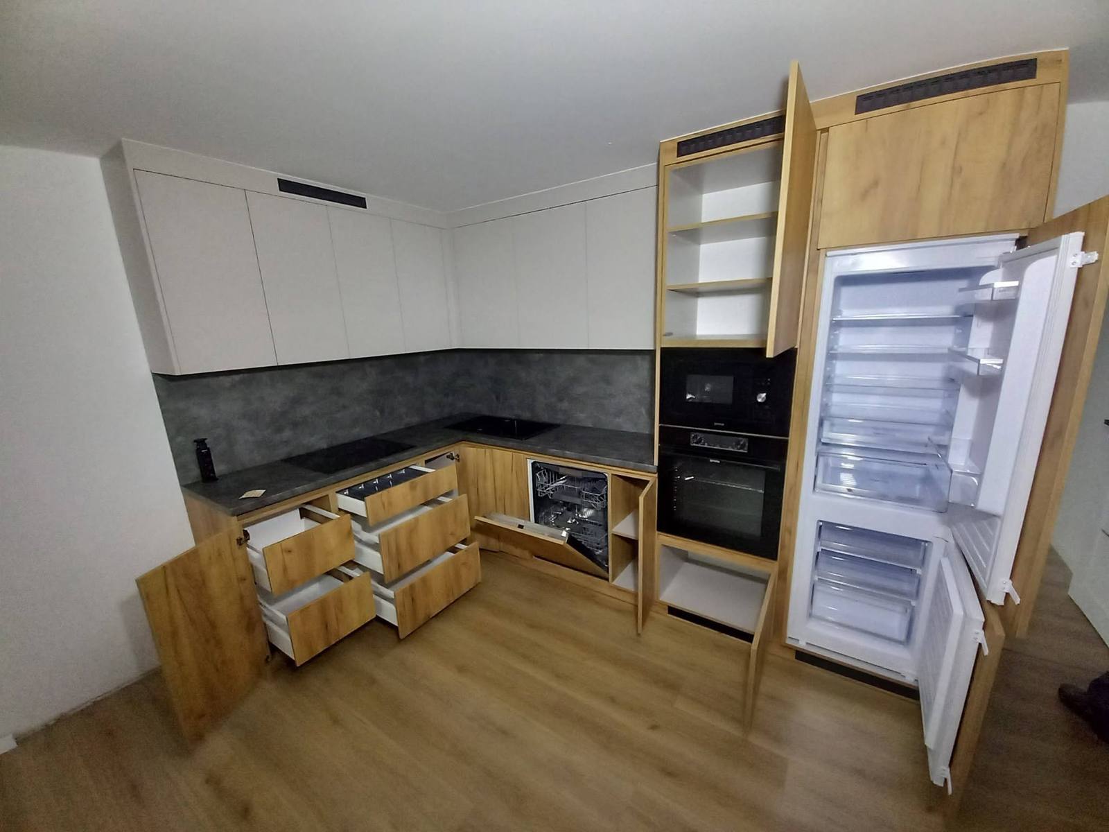 Küche mit geöffneten Schubladen und Einbaukühlschrank am dunklen Spiegel.