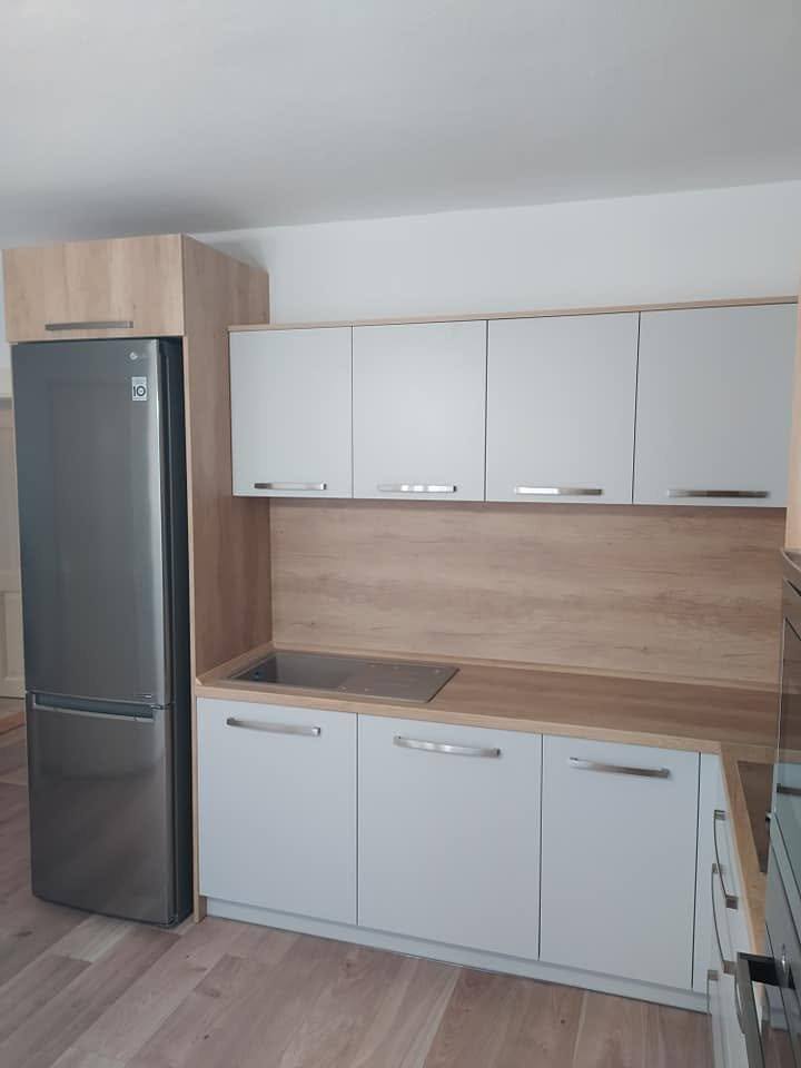 Weiße Küche mit Eichendekor-Rückwand und freistehendem Edelstahl-Kühlschrank