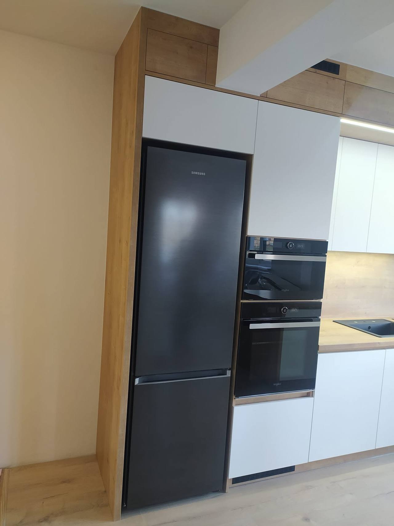Weiße Küche mit Eichendekor-Panel neben schwarzem Kühlschrank