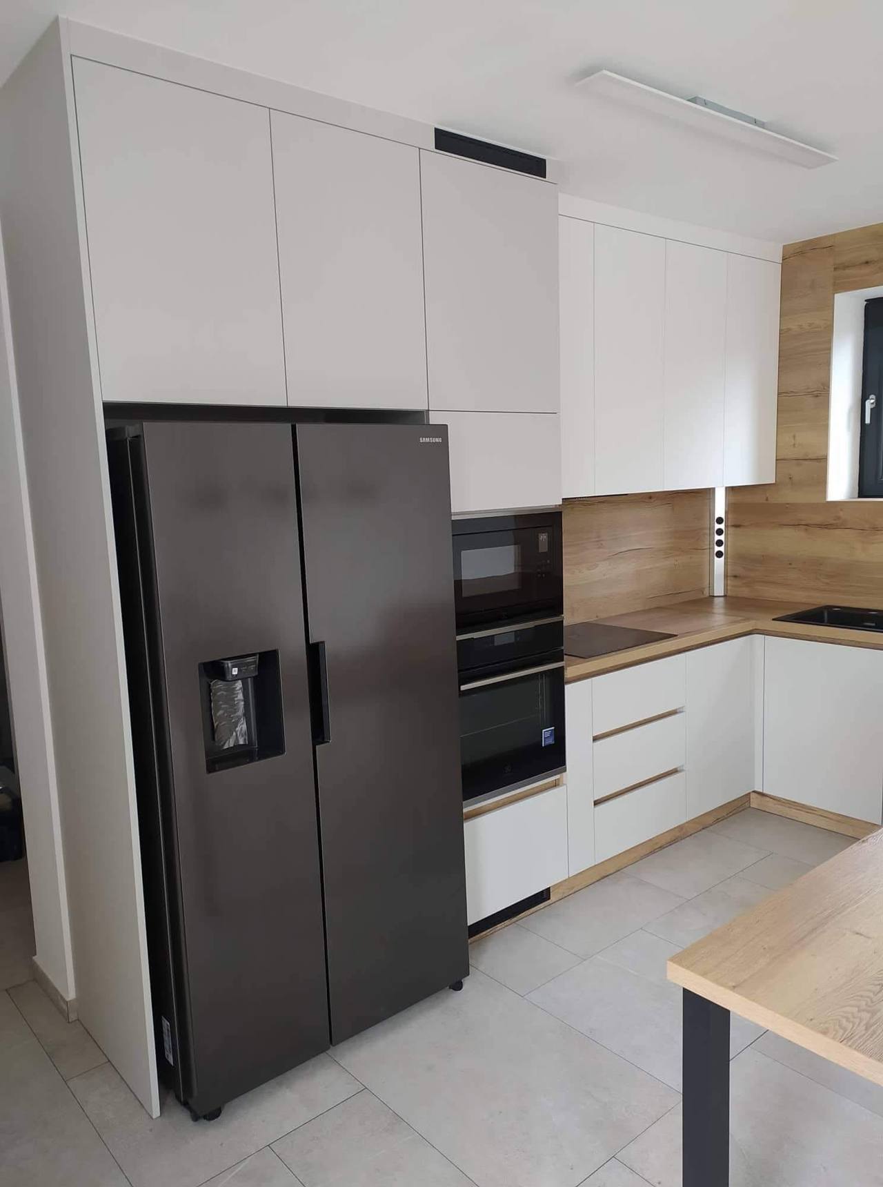 Weiße Küche mit hohem Schrank und schwarzem Side-by-Side-Kühlschrank