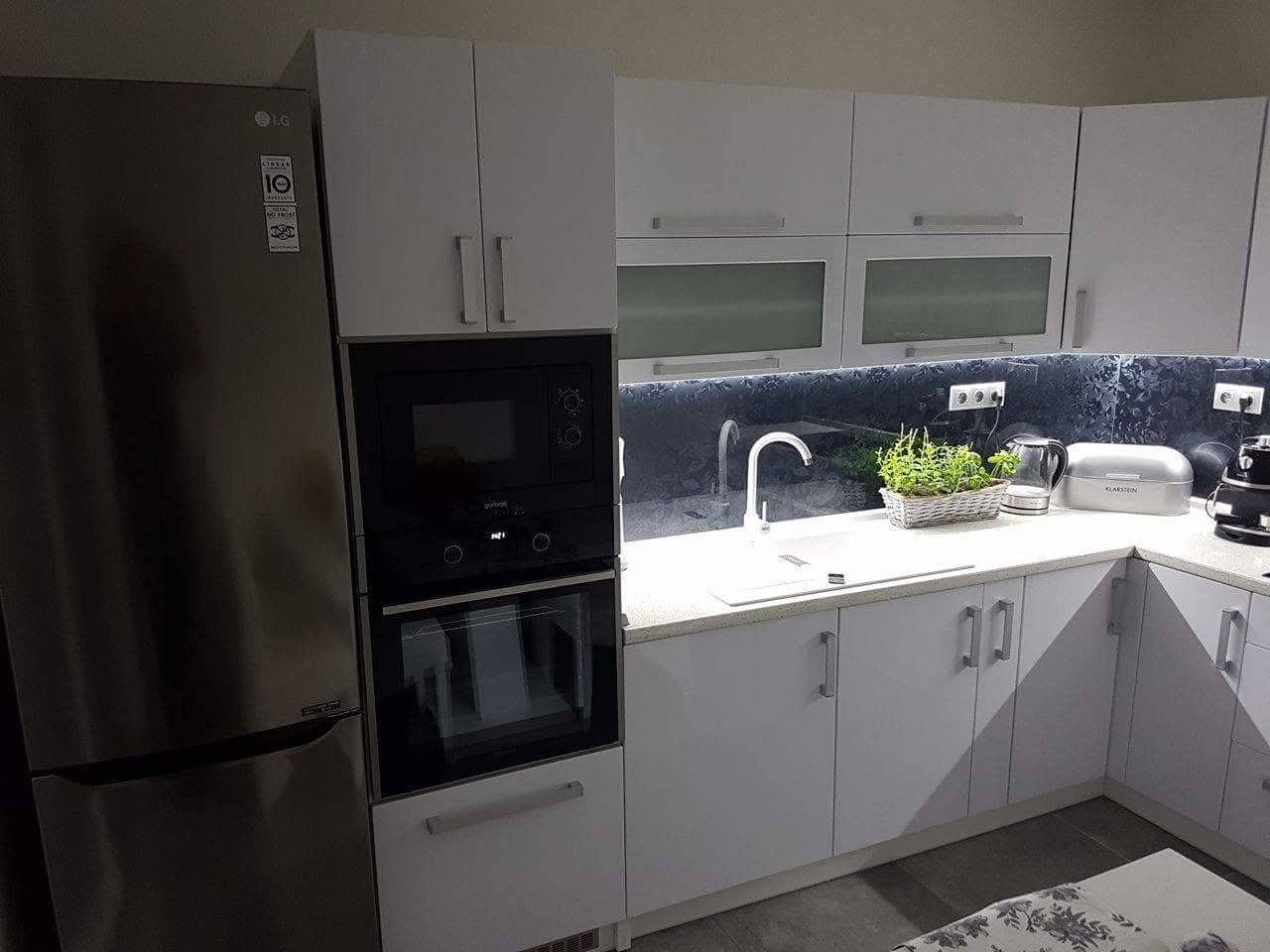 Weiße Küche mit dunkler Marmoroptik-Rückwand und hohem Kühlschrank