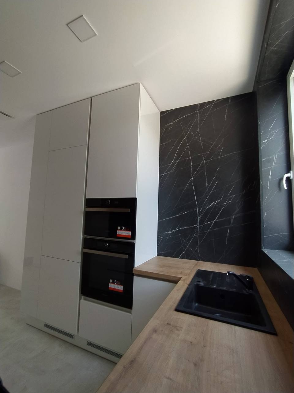 Weiße Küche mit hoher Schrankwand und dunkler Marmoroptik-Wand
