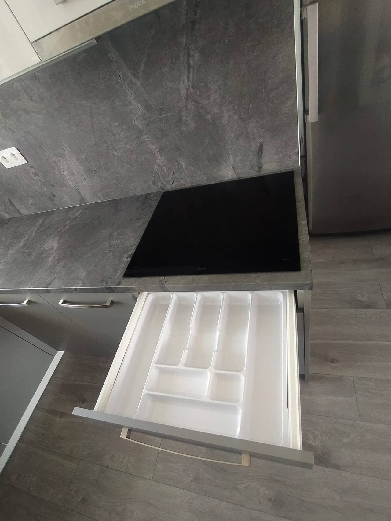 Ausgezogene Schublade mit weißem Besteckeinsatz unter der grauen Platte.