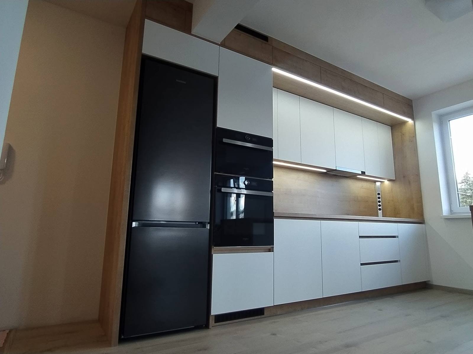 Weiße L-Küche mit schwarzem Hochkastenblock und Eichen-Rückwand
