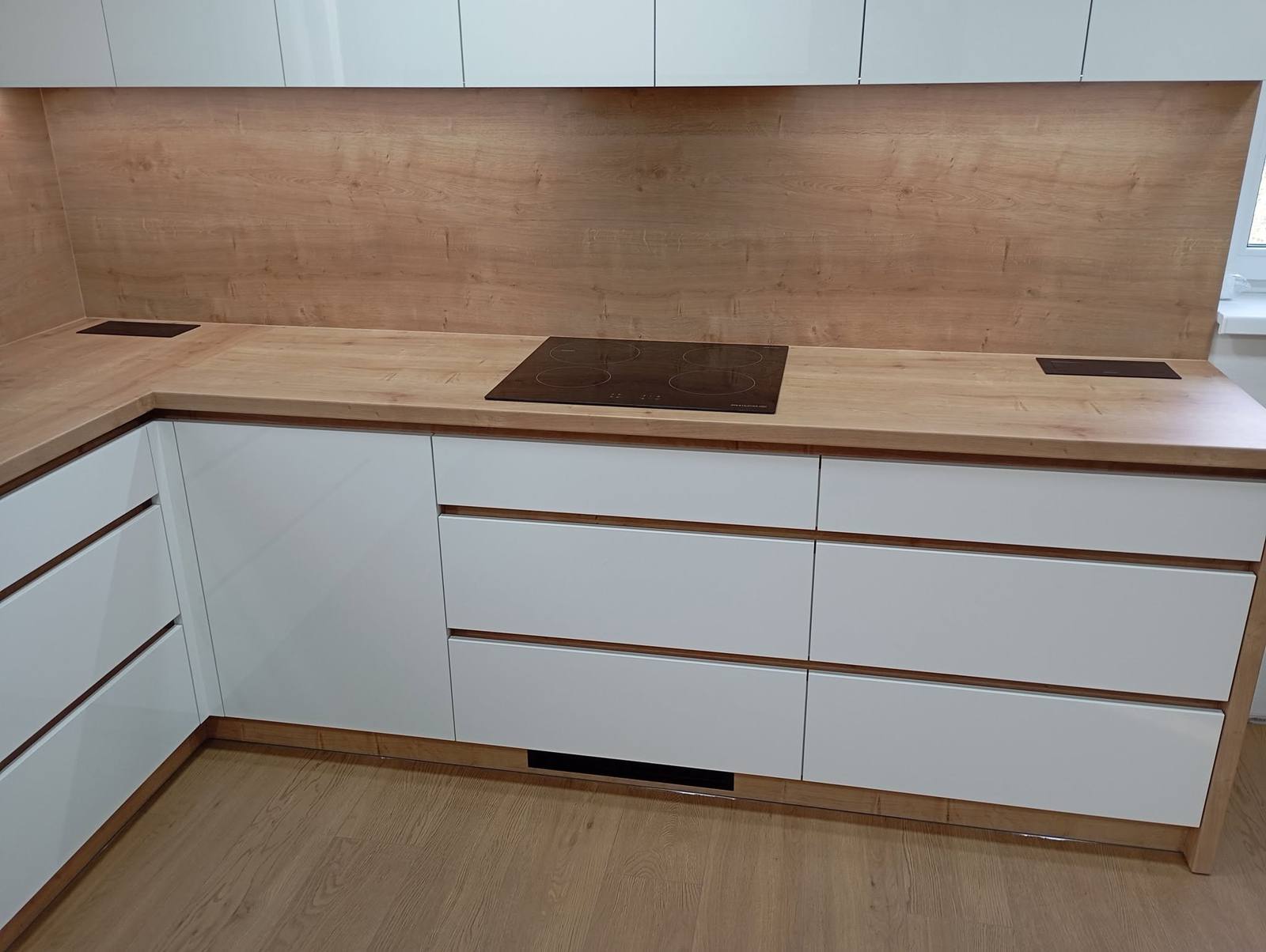 Weiße L-Küche mit Eichen-Arbeitsplatte und Wandspiegel.
