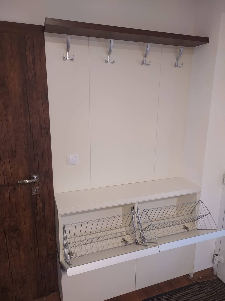Weiße Sitzbank mit zwei Klapp-Drahtkörben für Schuhe unter der Garderobe.