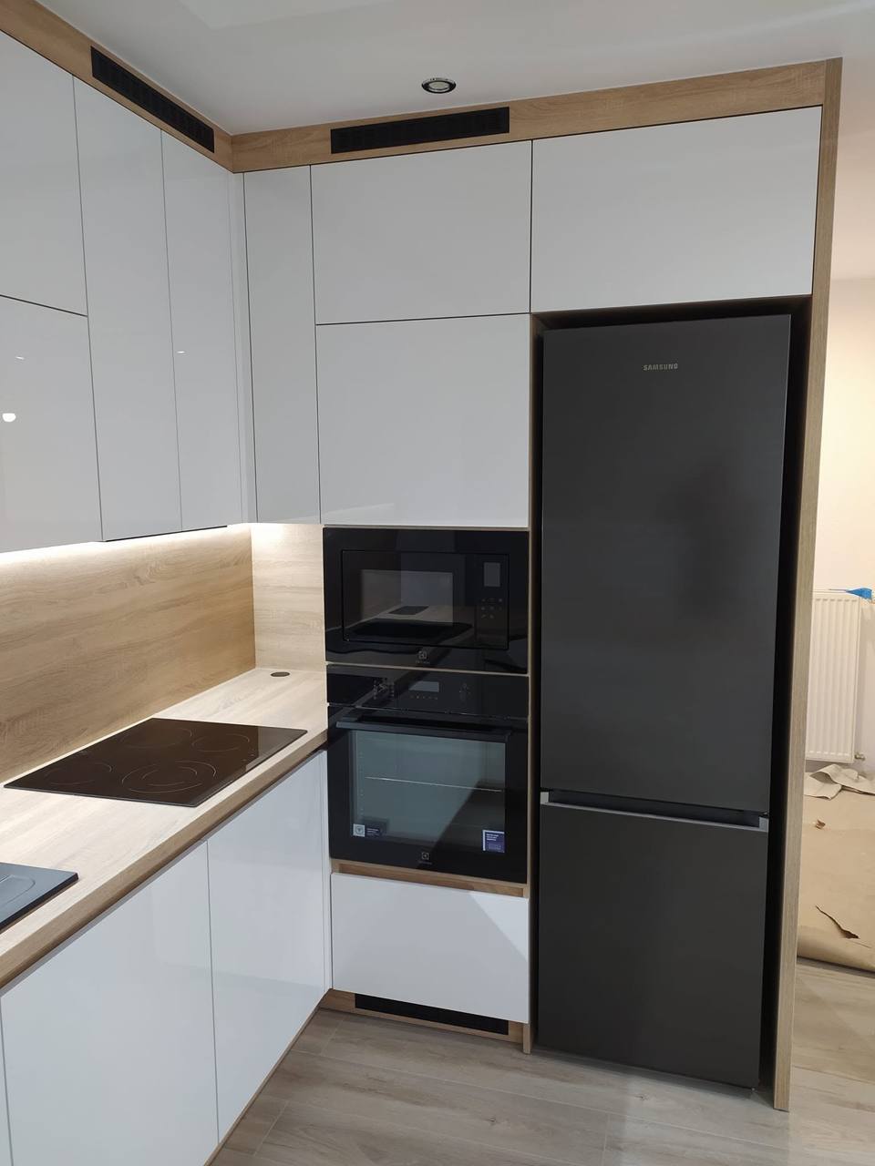Weiße Hochglanzküche mit schwarzem Kühlschrank und beleuchteter Rückwand