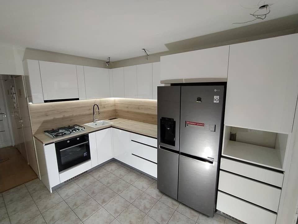 Weiße Hochglanzküche mit Eichenplatte und großem Kühlschrank.