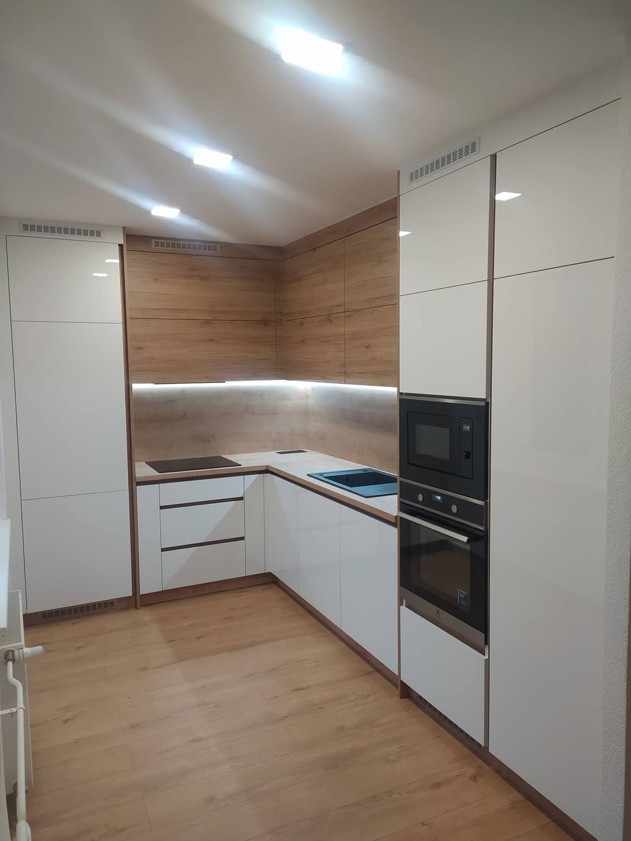 Blick auf die weiße Küche mit Hochkästen und Eichenwand