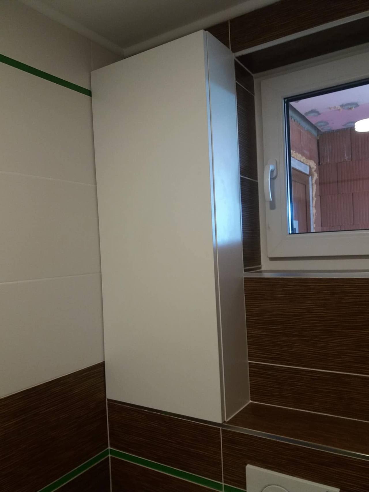 Hoher weißer Badschrank am Fenster mit dunkler Verkleidung
