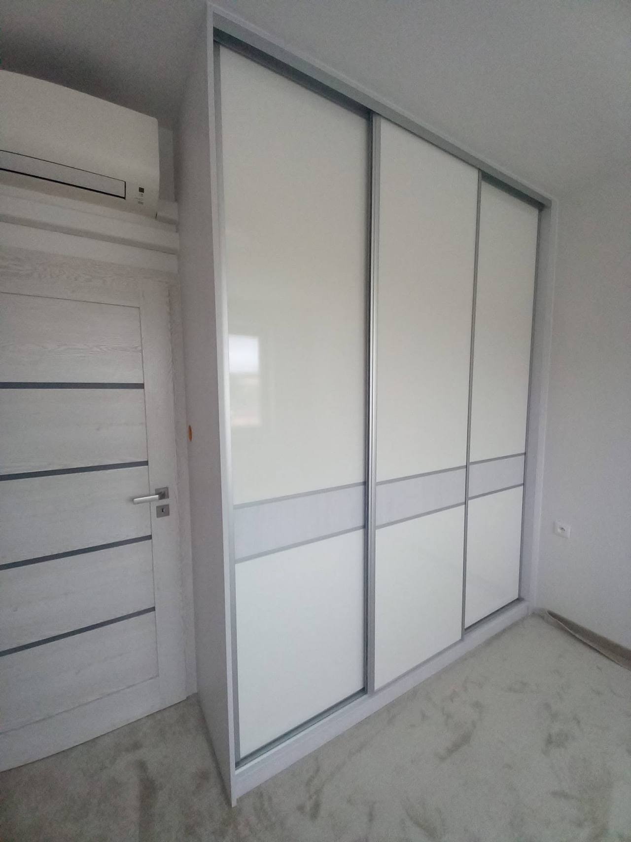 Biela posuvná skriňa so sivým pásom pod klimatizáciou