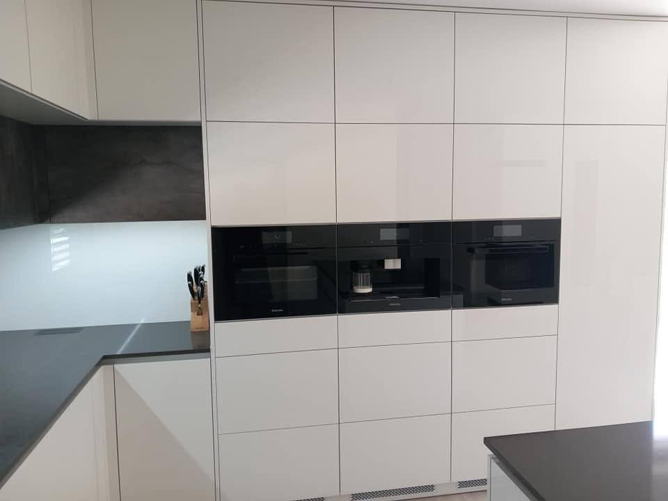 Weiße Hochglanz-Kastenwand mit schwarzen Geräten und dunkler Platte