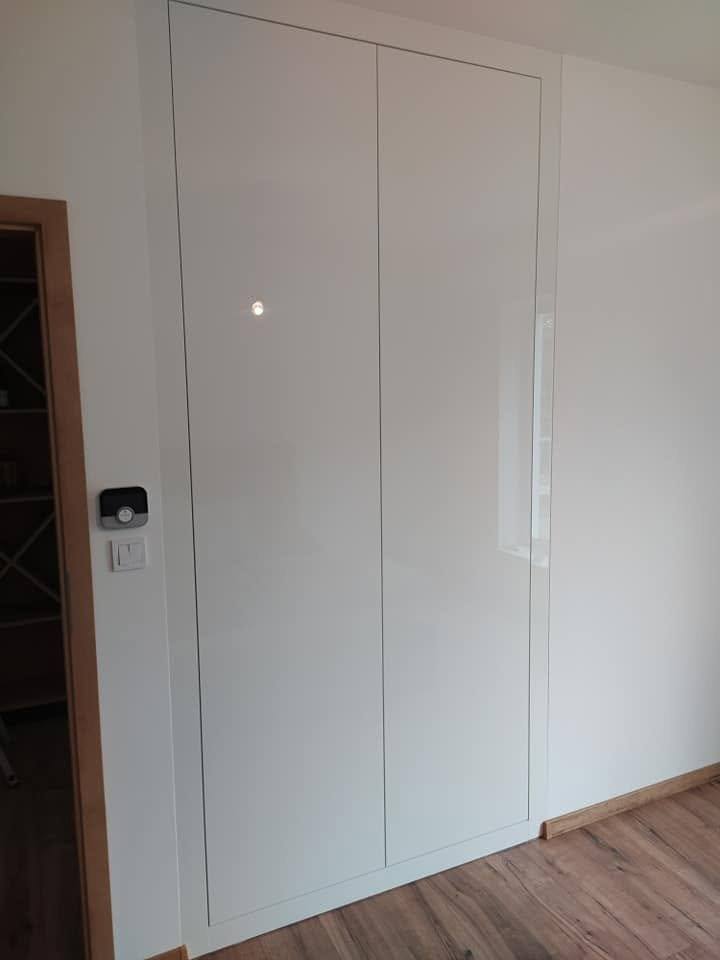 Biela lesklá skriňová stena vo vestibule pri dverách.