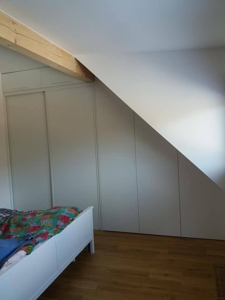 Weißer Kasten unter der Schräge neben dem einfachen Bett.
