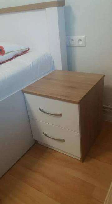 Nočný stolík v dekore dub s bielymi zásuvkami pri posteli