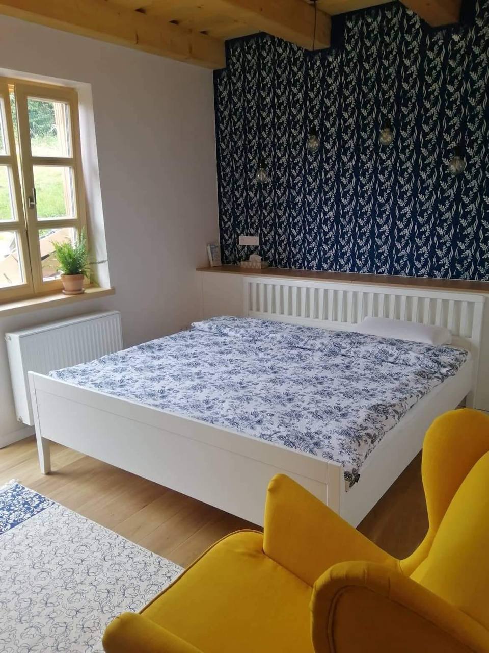 Biela manželská posteľ na nožičkách pod dreveným trámovým stropom