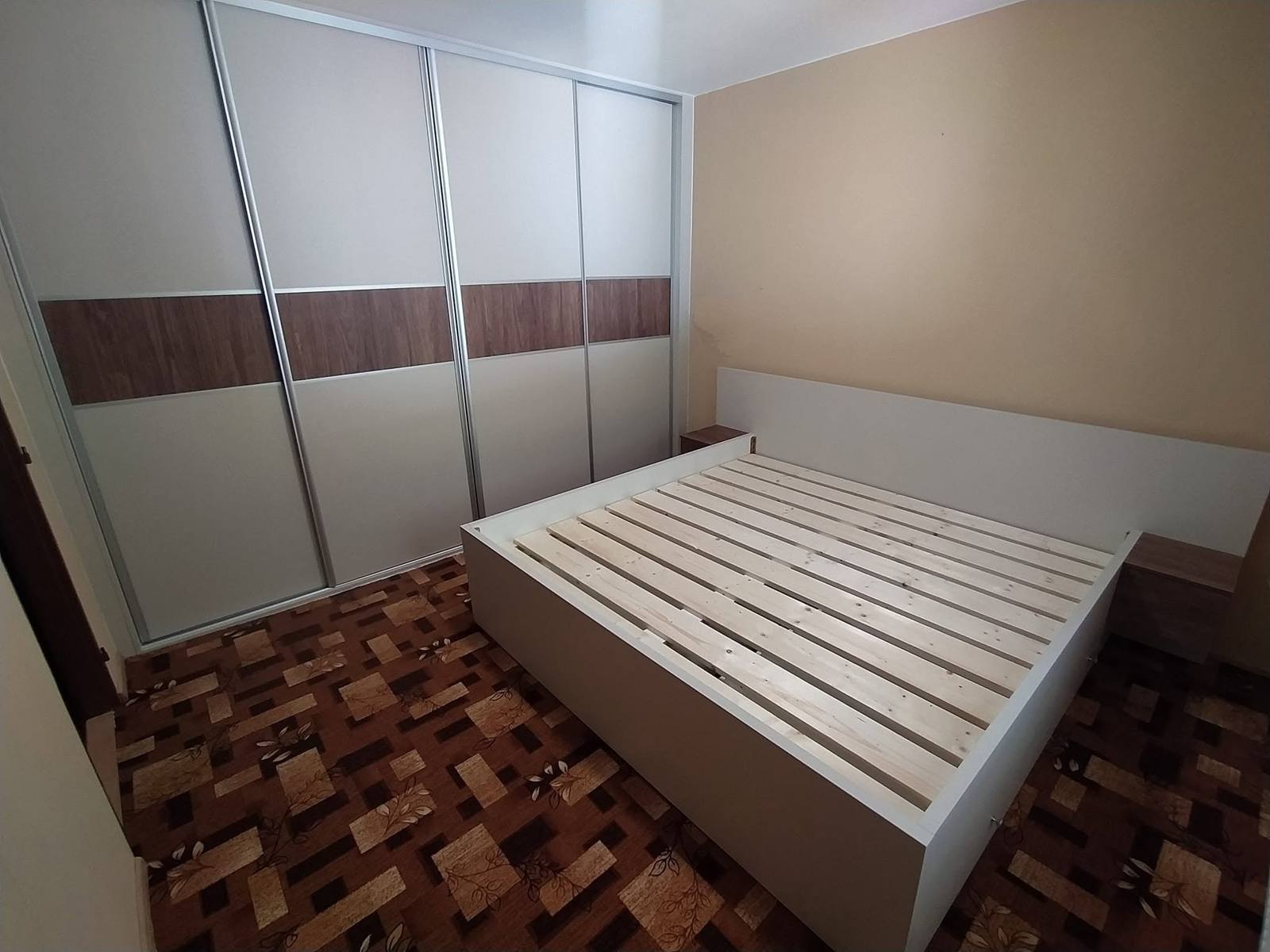 Posuvná skriňa s orechovými pásmi a biela posteľ v spálni