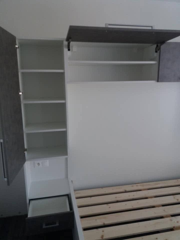 Geöffneter Seitenkasten mit Fachböden und Klappe über dem Bett