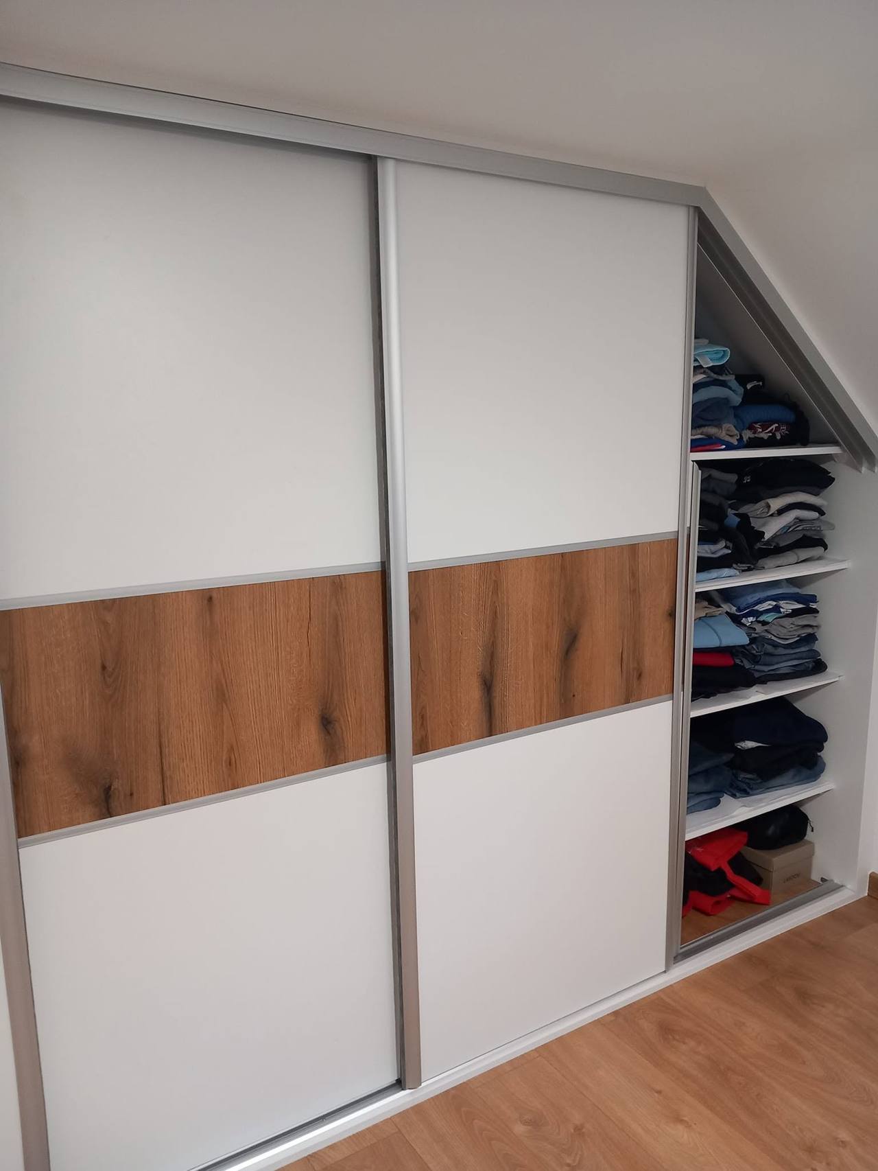 Weißer Schiebetürkasten mit Eichenband und Seitenregalen unter der Dachschräge.