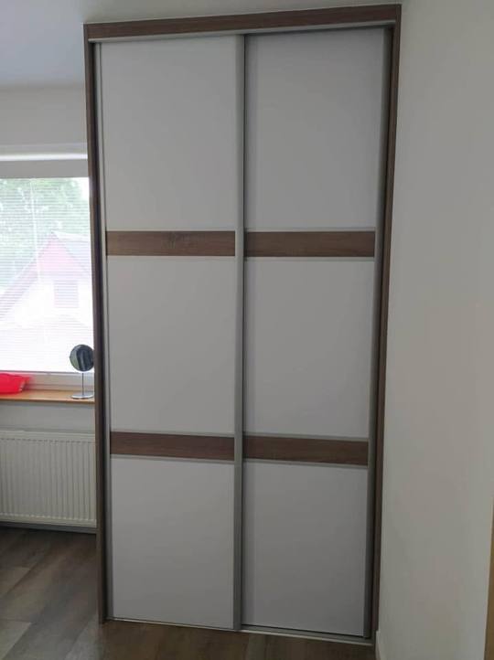 Biela posuvná skriňa s horizontálnym pásom v dekore orech naprieč dverami.