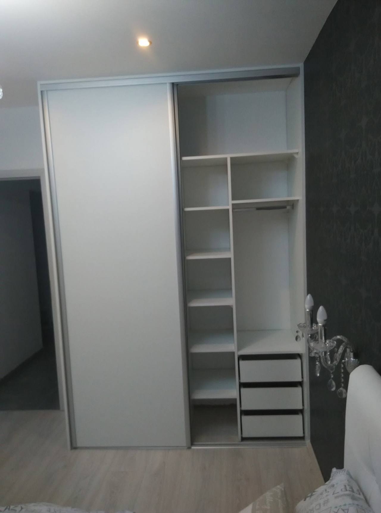 Halb offener weißer Kasten mit Fachböden und Laden neben dunkler Tapete