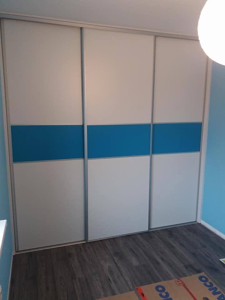 Weißer Schiebetürenkasten mit blauem Band vor hellblauer Wand
