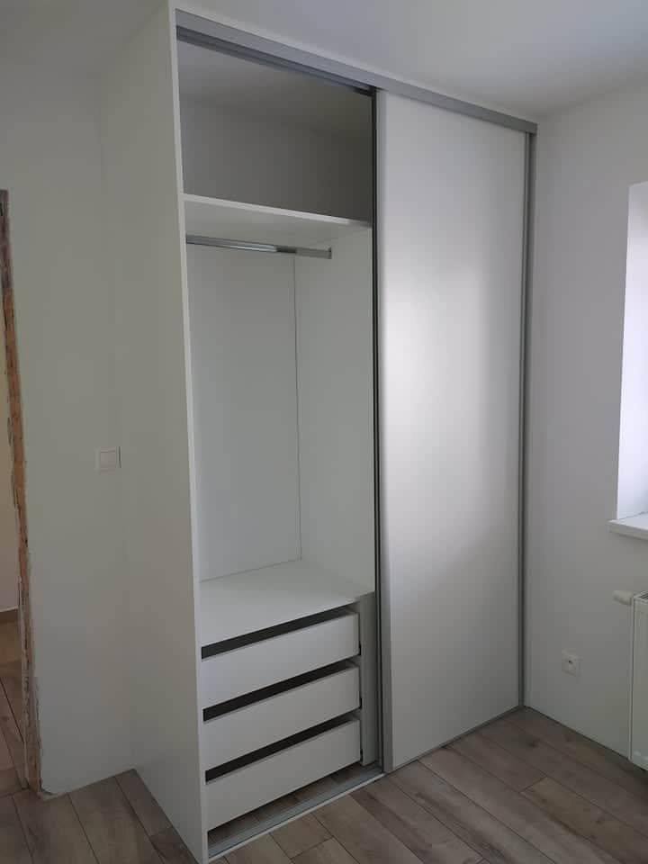 Inneres eines weißen Schwebetürenkastens mit Kleiderstange und Laden