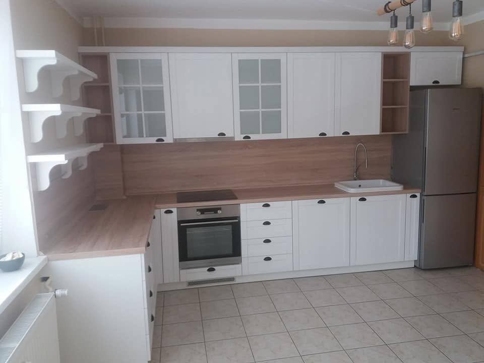 Gesamtansicht der weißen L-Küche mit Kühlschrank und Wandborden