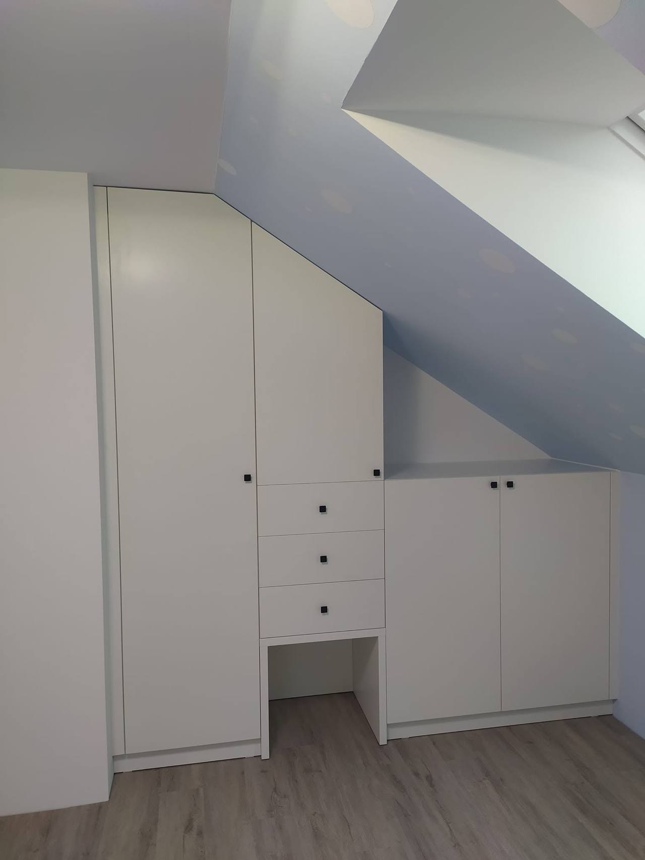 Hohe weiße Kästen und Laden mit schwarzen Knöpfen unter dem Dachfenster