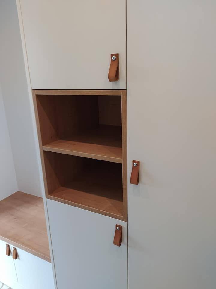 Biela skriňa s otvorenou nikou v dekore dub a koženými pútkami na dvierkach.