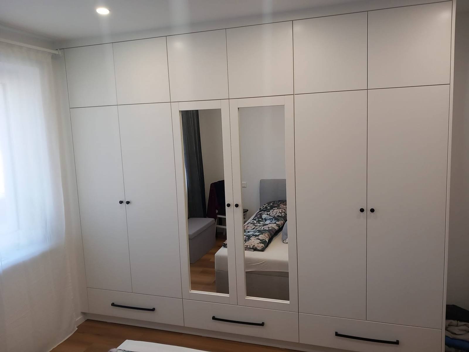 Breite weiße Kastenwand mit Spiegeln und schwarzen Griffen