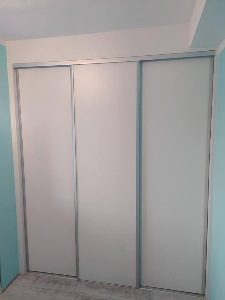 Weißer dreitüriger Schwebetürenschrank im schlichten Zimmer
