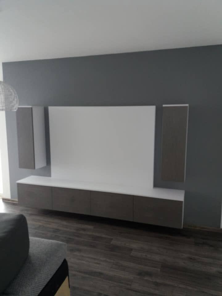 Weiße TV-Wand mit hohen grauen Kästen vor dunkelgrauer Wand