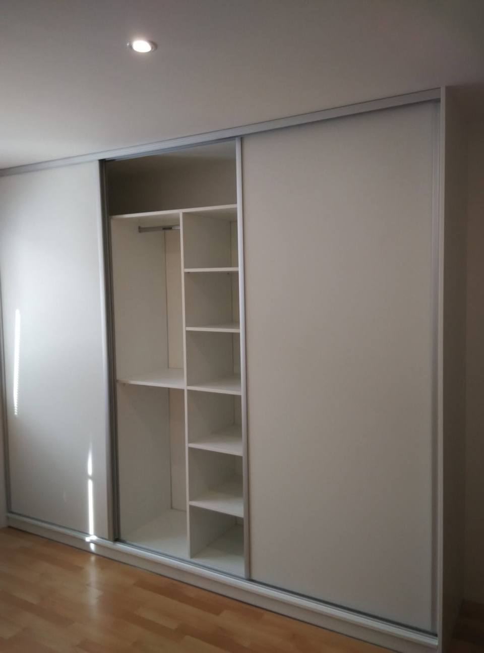 Weißer Einbaukasten mit offenen Fachböden und Kleiderstange.