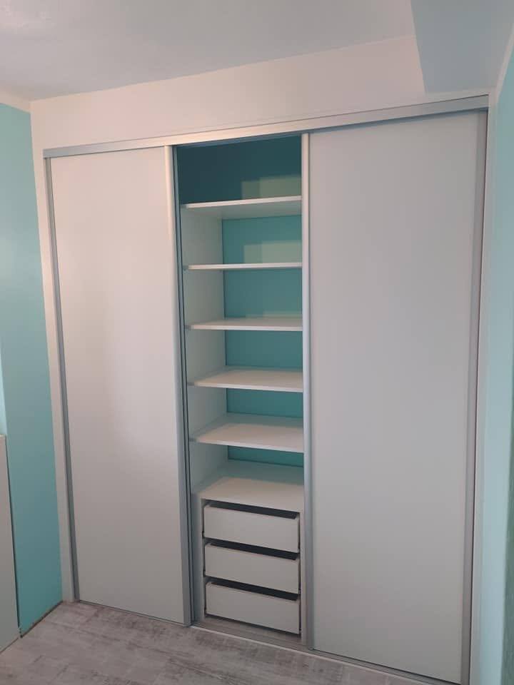 Weißer Einbaukasten mit Böden und Schubladen an türkisfarbener Wand.