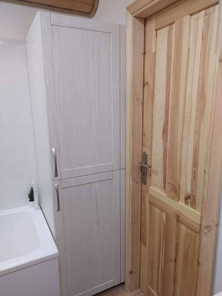 Hoher weißer Badschrank neben der Kiefertür aus anderem Winkel