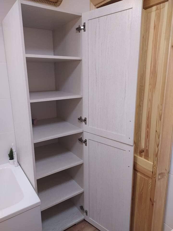 Offener weißer Badschrank mit Regalen neben der Kiefertür