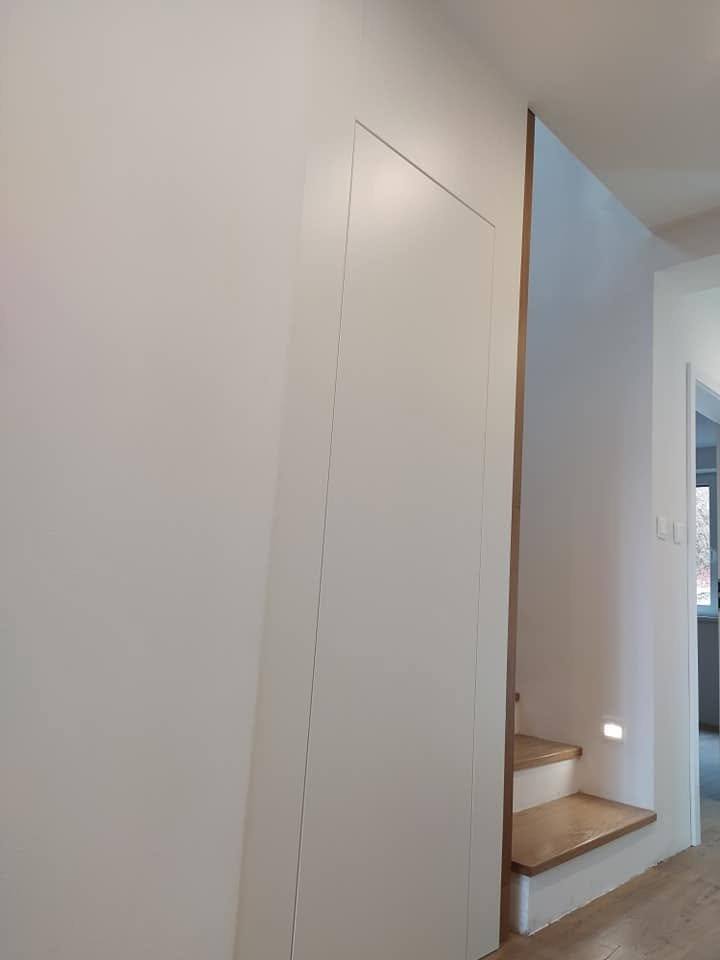 Weiße verdeckte Tür in der Wand neben der Stiege