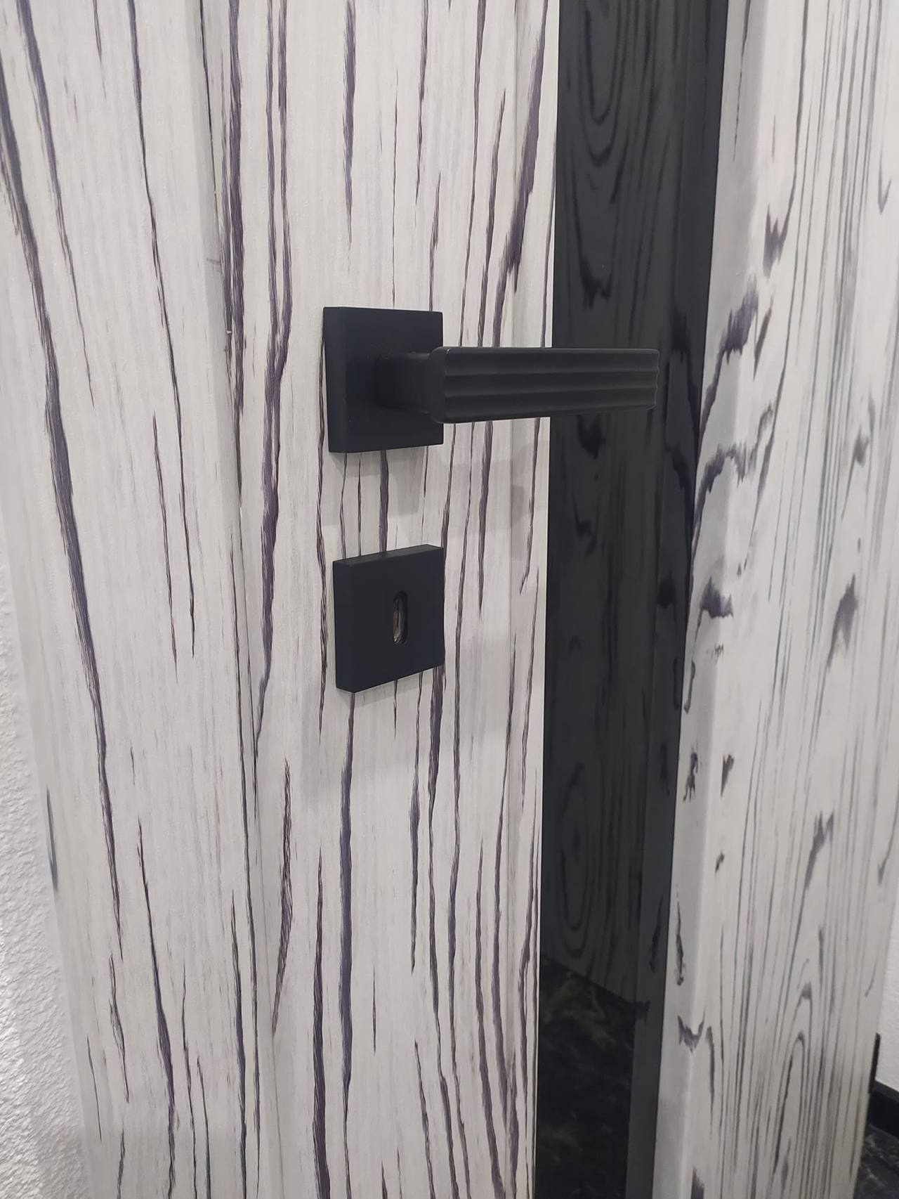 Schwarze Klinke an der Tür mit kräftiger Holzmaserung